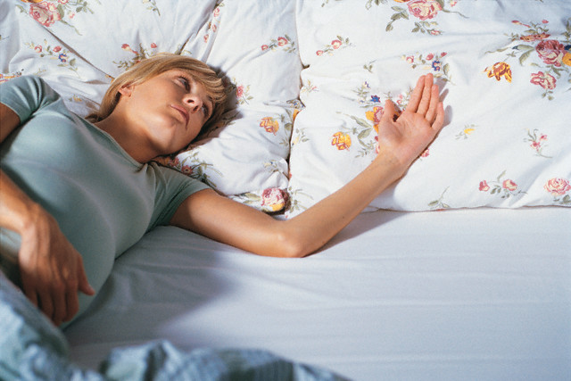 Pregnant woman looking at the empty space on the bed next to her